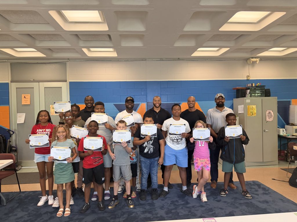 Young people holding certificates alongside adults in a community room.